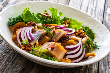 Marinated herrings with delicacies, walnuts and fresh vegetable leaves on wooden table
