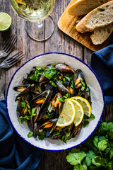 Cooked mussels with lemon and parsley on wooden table
