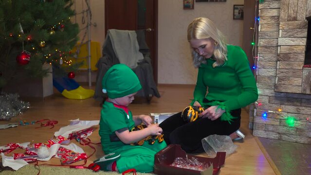 Kid In Grinch Costume. Mom Helps Open Christmas Gifts