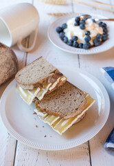 Healthy breakfast sandwich with sourdough bread and quark cheese. Served with a fresh yogurt and berries on white background 