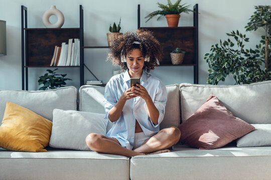 Young woman surfing net using mobile phone sitting on sofa at home