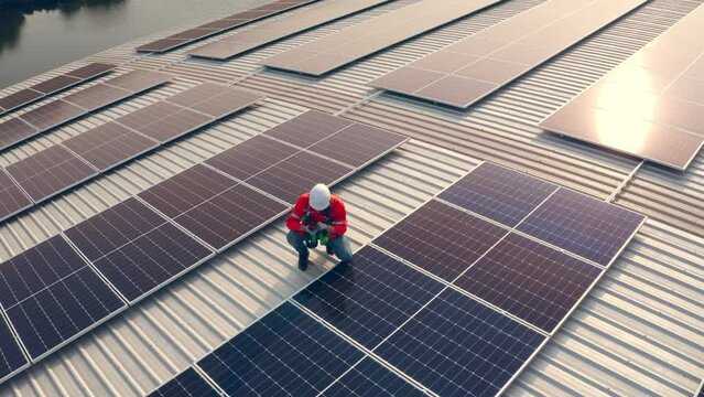 Drone shot, Male engineer maintaining solar cell panels on building rooftop. Technician working outdoor on ecological solar farm construction. Production of renewable energy concept.