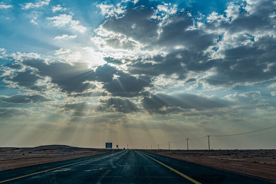 Saudi Arabia, Al-Ula, Setting sun piercing clouds over empty highway