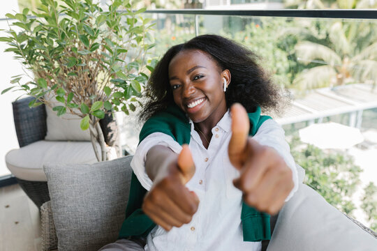 Happy woman showing thumbs up gesture sitting on sofa on balcony