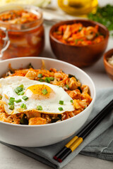 Kimchi cabbage with rice and chicken. Served in a white bowl on a light marble background.