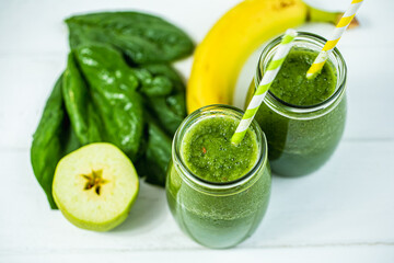 From above view of glasses jars filled with green smoothie and ingredients on wooden table. 