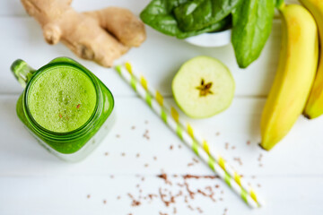  Top down view of mason jar mug filled with green smoothie and ingredients on wooden table. 