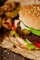 Closeup juicy beef burger with french fries, vegetables, cheese on rustic table. Homemade cooking