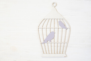 Silhouette of a cage with birds made of wood on a light wooden background