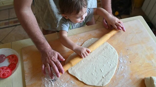 Little boy assisting father rolling out fresh pizza dough