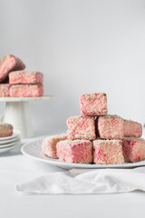Pink lamingtons on a ceramic plate Australian raspberry lamingtons, small cakes covered in desiccated coconuts