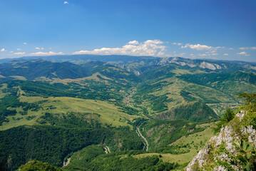 Naklejka premium Rural idyllic landscape with grassy fields and rolling hills, sunny afternoon. Wonderful springtime landscape in mountains. Beautiful scenery with forests, hills, meadows and village in distant valley