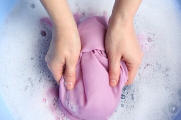 Top view of woman hand washing color clothing in suds, closeup