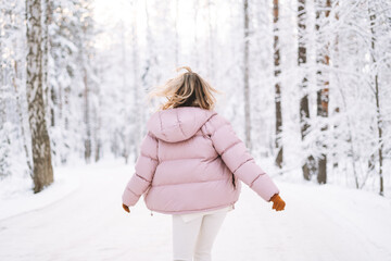 Blurred photo of young blonde woman in winter clothes walking in snowy winter forest