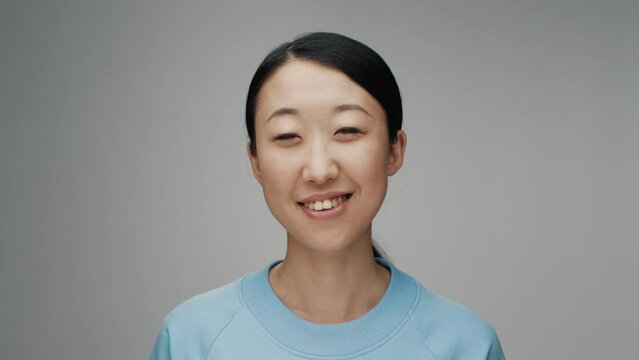 Portrait of Young Korean Woman Looking at Camera in Color Studio Shot. Adult Japanese Girl Isolated Alone on Grey Background Close up. Asian Person with Happy Friendly Face Smiling and Opening Eyes