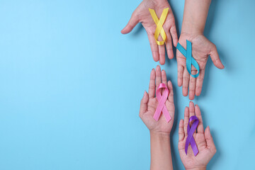 World cancer day. Hands of people open and holding colorful awareness ribbons forming circle as...