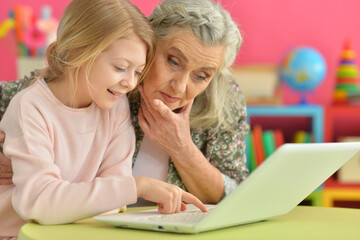 little girl with her grandmother using modern laptop