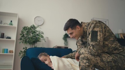 Young male soldier taking care of his sleepy daughter, covering with a blanket