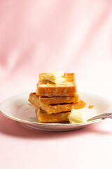 Front vertical view of a pile of belgian waffles with white chocolate on a pink background