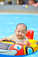 Portrait of cheerful cute baby smiling while swimming using colorful inflatable float at pool