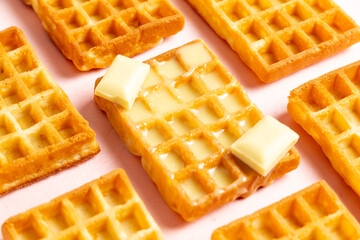 Diagonal close up view of belgian waffles with white chocolate on a pink background