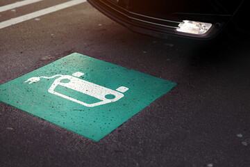 parking lot scene with car entering a section marked with symbol of a car with cable plug painted...