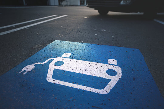 parking lot with symbol of a car with cable plug painted on asphalt in blue and white. electric vehicle charging station with entering car. electro mobility concept. selective focus