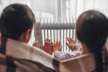 Shutdown of heating and electricity, blackout. Children warm their hands from a battery powered by...