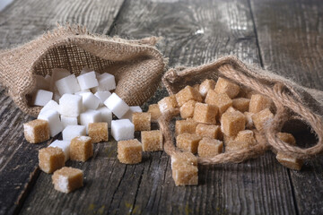 Pieces of white and brown sugar lie in bags on a wooden table.  Different refined sugar cubes on wooden background