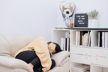 Young Asian woman feeling depressed laying in sofa burying her face in hands and crying. Teen girl...
