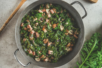 Stewed kale with mushrooms in cooking pot. Healthy green food. Top view - obrazy, fototapety, plakaty