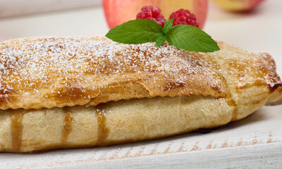 Baked strudel with apples sprinkled with powdered sugar on a white wooden board, delicious dessert