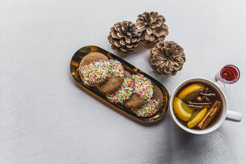 Sugar cookies covered halfway with colorful sprinkles standing next to winter tea with orange and cinnamon. Top view. High angle shot. High quality photo