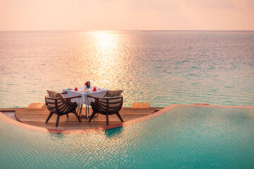 Seascape view under sunset light with dining table with infinity pool around. Romantic tranquil getaway for two, couple concept. Chairs, food and romance. Luxury destination dining, honeymoon template