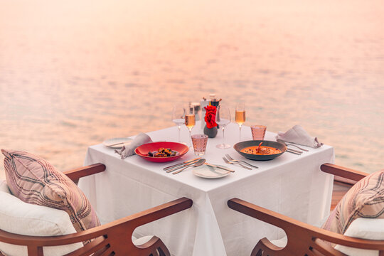 Seascape view under sunset light with dining table with infinity pool around. Romantic tranquil getaway for two, couple concept. Chairs, food and romance. Luxury destination dining, honeymoon template