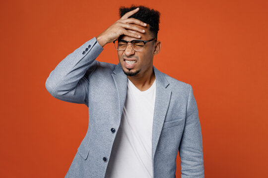 Young employee business man corporate lawyer in classic formal grey suit shirt glasses work in office put hand on face facepalm epic fail mistaken omg gesture isolated on plain red orange background