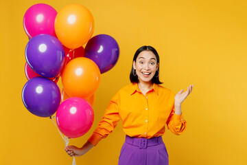 Fototapeta na wymiar Happy fun surprised shocked young woman wearing casual clothes celebrating holding bunch of colorful air balloons spread hands isolated on plain yellow background. Birthday 8 14 holiday party concept.