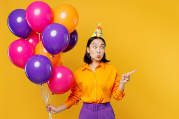 Fototapeta na wymiar Happy fun happy young woman wear casual clothes hat celebrating hold bunch of colorful air balloons point finger aside on area isolated on plain yellow background. Birthday 8 14 holiday party concept