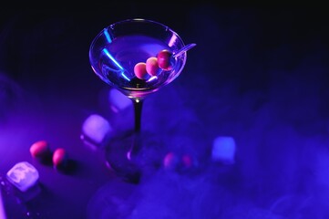 Glass of classic dry martini cocktail with olives on dark table against black background. With free...