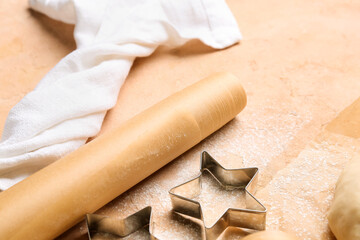 Roll of baking paper and cookie cutters on beige table, closeup