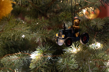 Christmas background: close-up of traditional nostalgic vintage wooden decoration (bear on a tractor) on blue spruce with lights in a living room with copy space