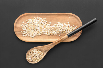 Wooden board and spoon with raw oatmeal on dark background