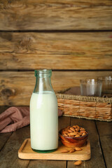 Board with bottle of almond milk and nuts on wooden table
