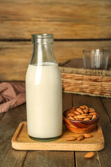 Board with bottle of almond milk and nuts on wooden table