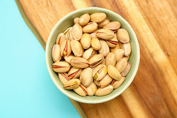 Cutting board and bowl with tasty pistachio nuts on blue background