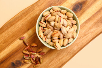 Cutting board and bowl with tasty pistachio nuts on beige background