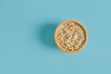 Wooden bowl with tasty oatmeal on blue background