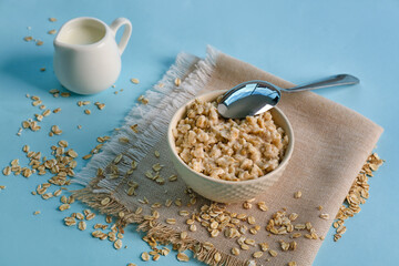 Bowl with tasty oatmeal, spoon and pitcher on blue background