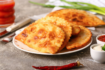 Plate with tasty chebureks and chilli pepper on grunge background