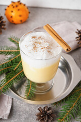 Glass of tasty eggnog cocktail and fir branches on grunge background